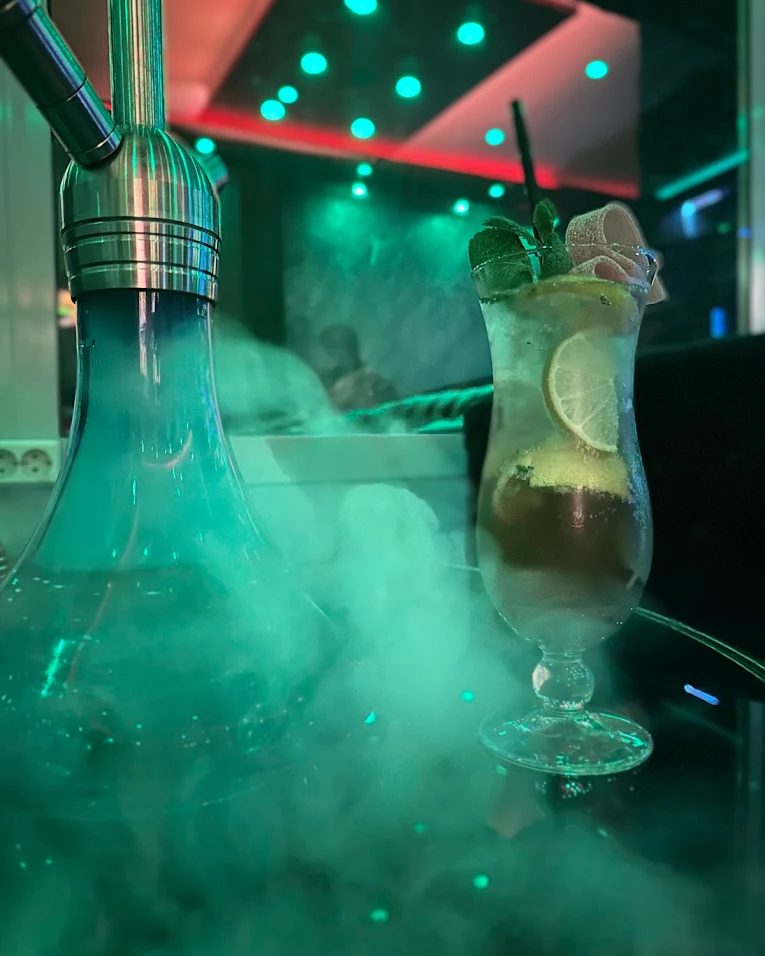 Mojito neben einer Shisha im Sternzeit, der Raum dahinter in grünem Licht und Nebel.
