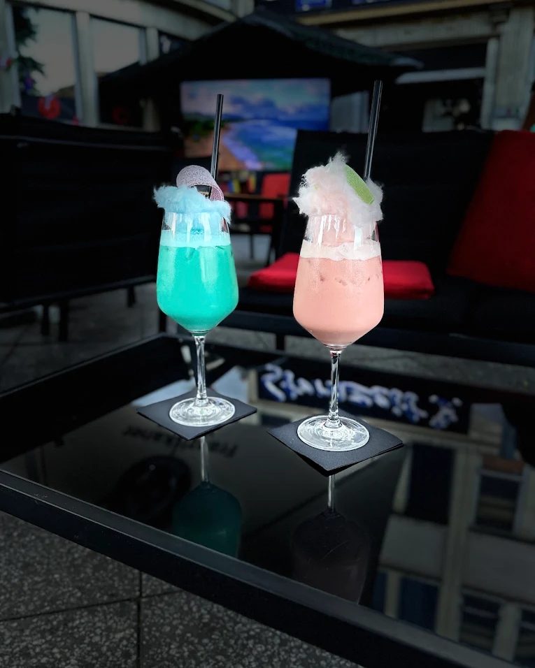 Zwei Cocktails auf einem Tisch im Sternzeit, im Hintergrund die Sitzecke und ein Bildschirm.
