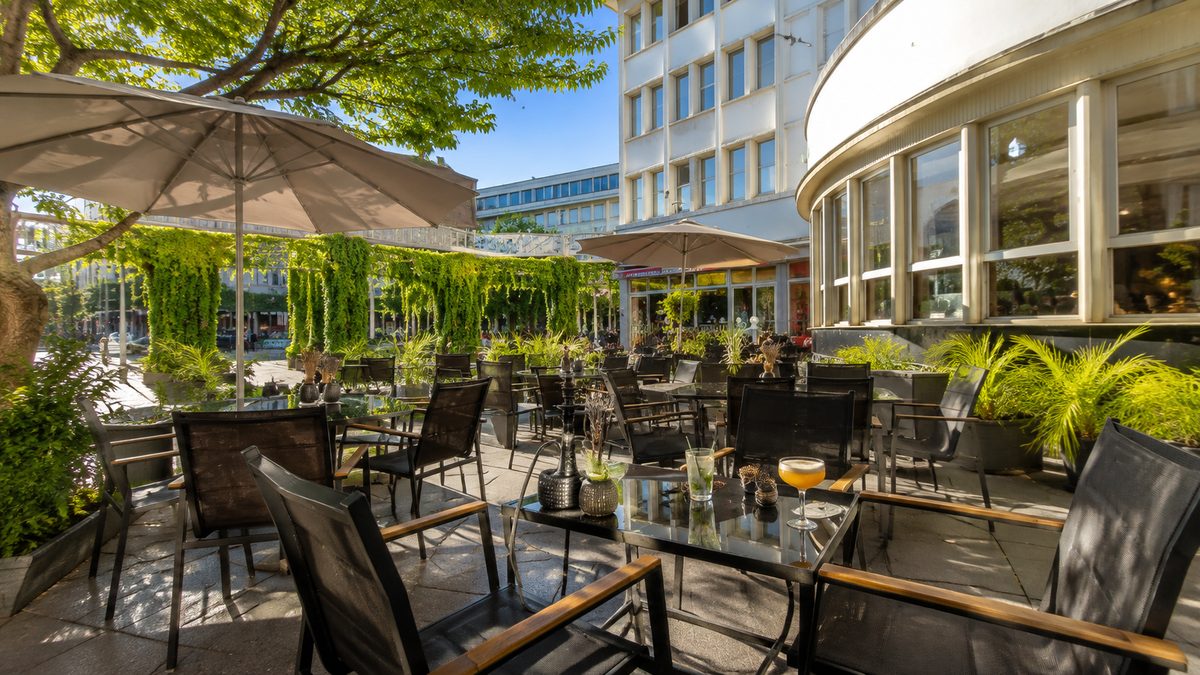 Die Terrasse des Sternzeit an einem sonnigen Tag: Sonnenschirme, begrünte Trennwände und Tische mit Drinks.