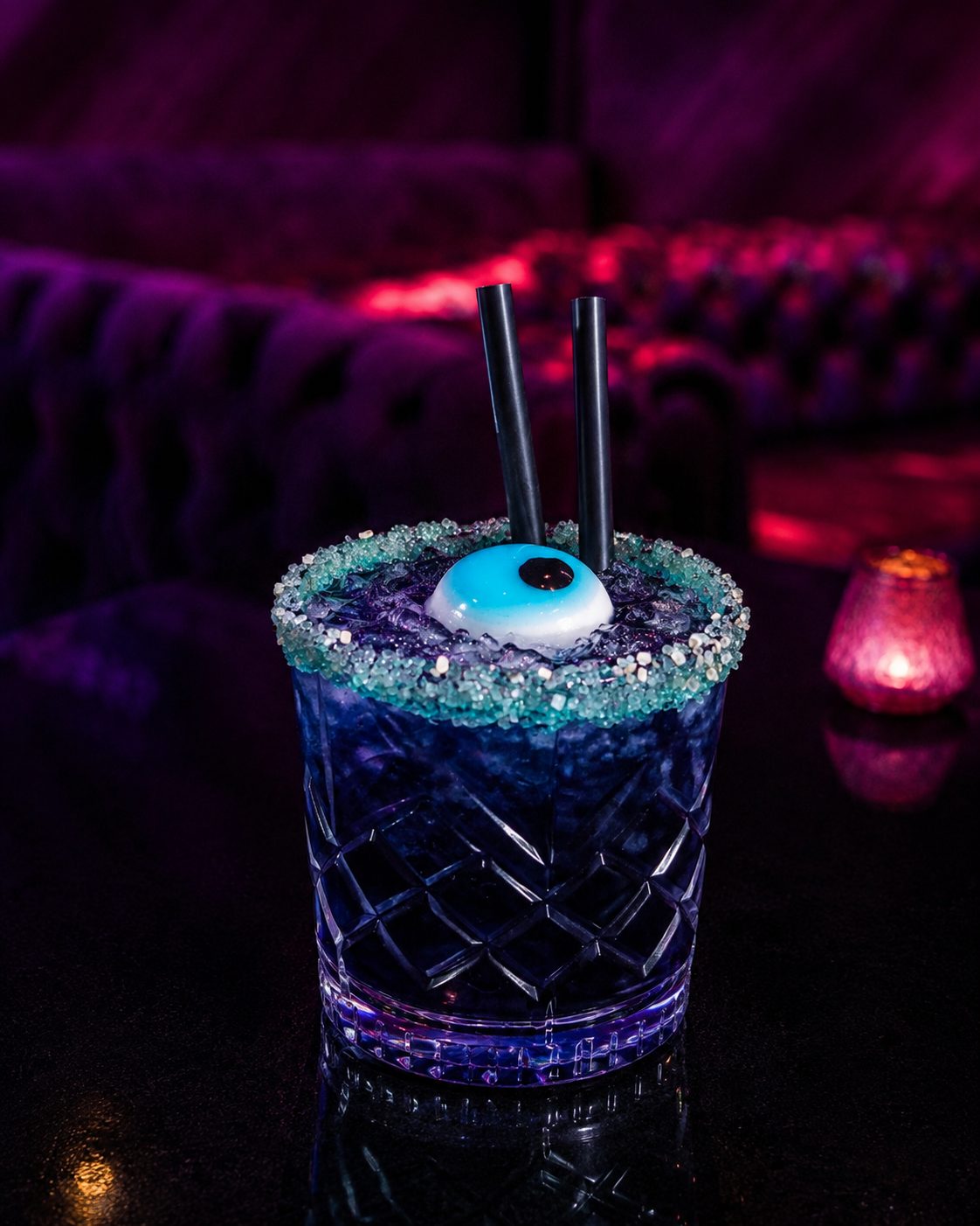 Blauer Cocktail im geschliffenen Glas mit türkisem Zuckerrand und auffälliger Garnitur, dahinter die Polsterbank im Sternzeit.