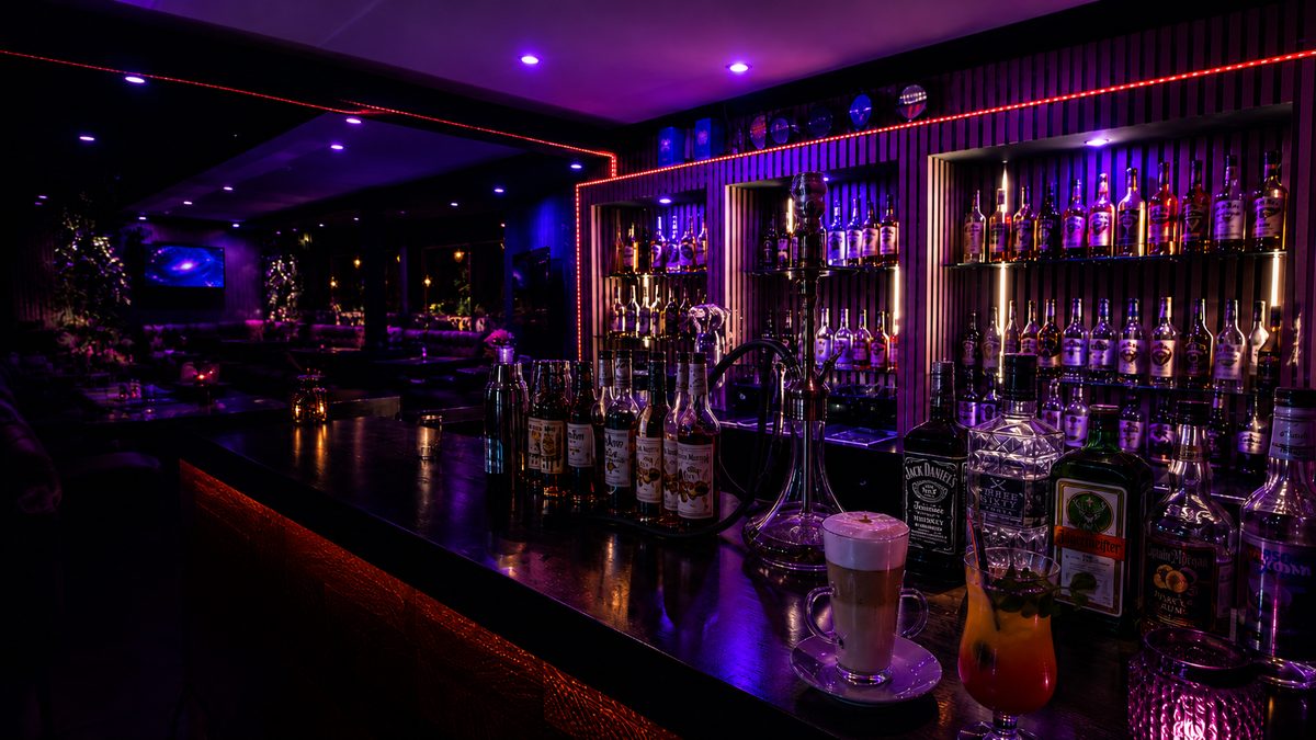 Die Bar im Sternzeit: Flaschenregal in blauem und violettem Licht, davor eine Shisha, ein Latte Macchiato und ein Cocktail auf dem Tresen.
